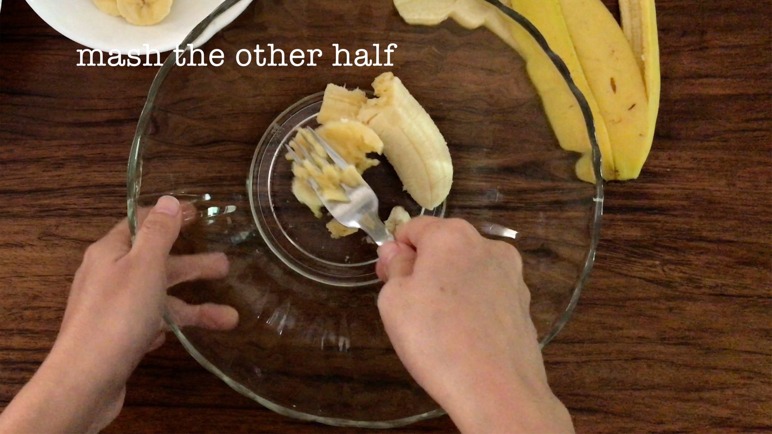 mashing half of a banana in a big glass bowl with a fork