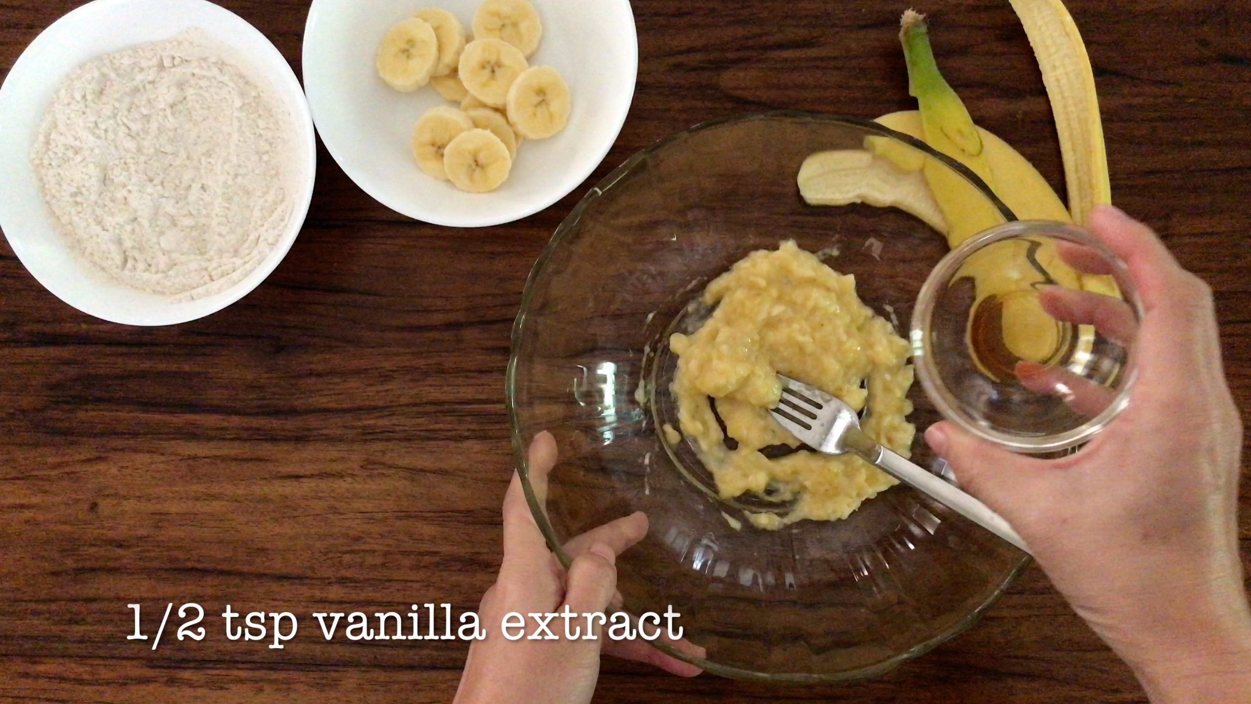 adding 1/2 tea spoon of vanilla extract in a big glass bowl with mashed banana