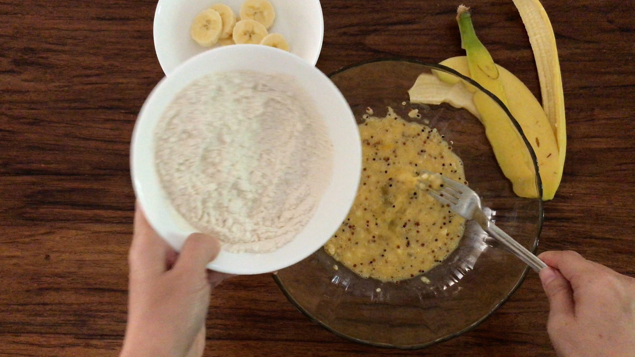 pouring flour mixture into a big glass bowl with the mashed banana mixture
